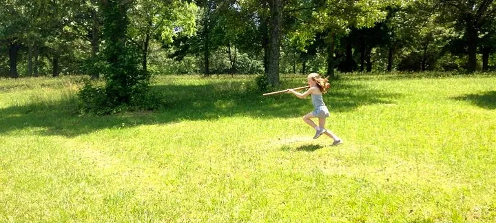 a little girl running through a field with a toy musket