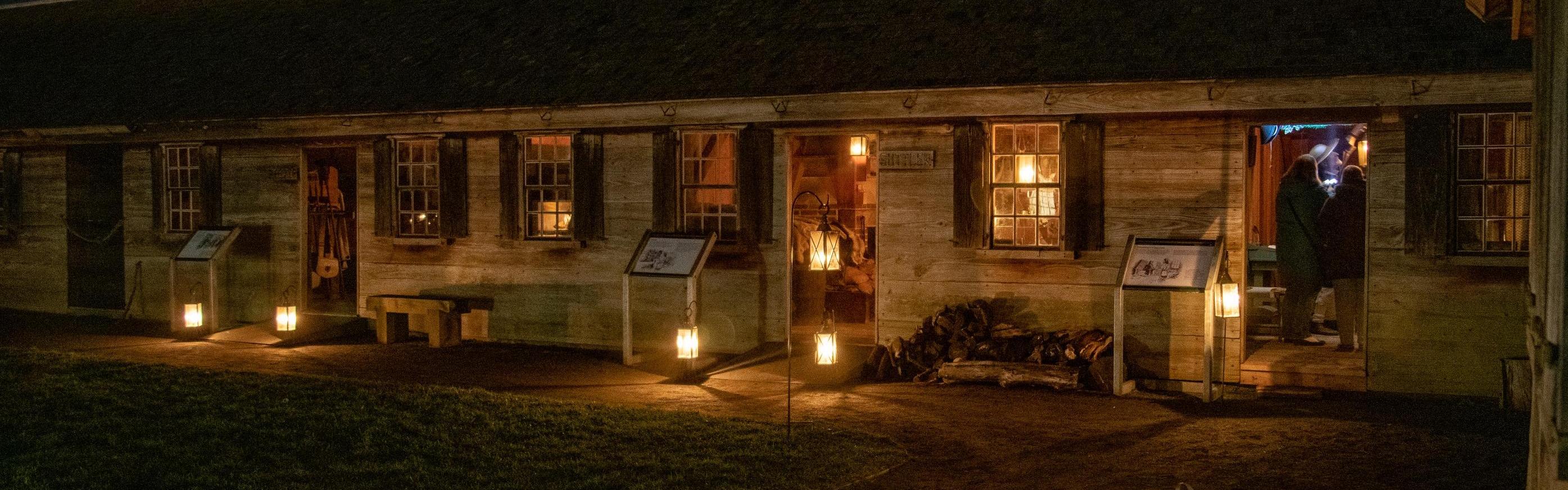 Candles in lanterns pour a golden light onto a darkened wooden building.