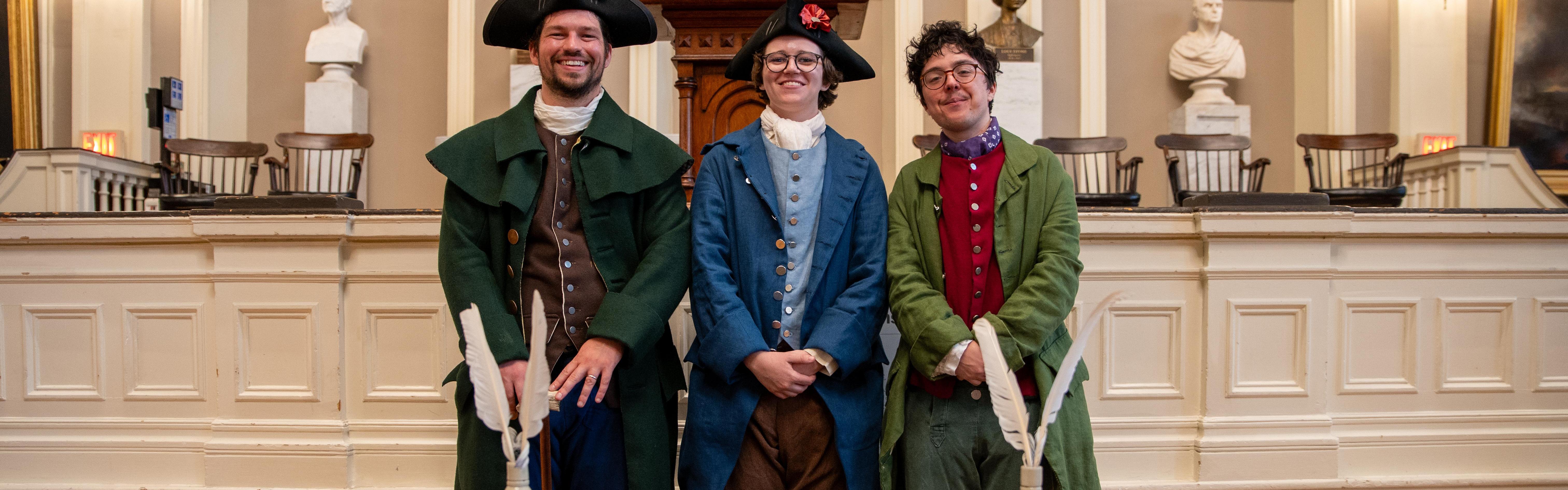 Three rangers in historic clothing stand in front of a signed resolution smiling at the camera