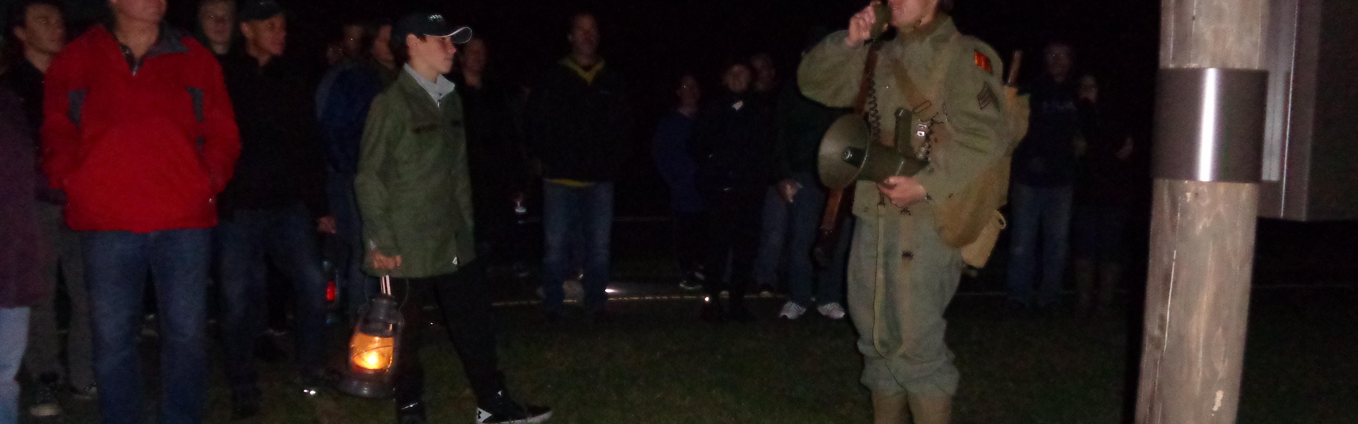 Man in WW II military uniform leading group of visitors holding lanterns