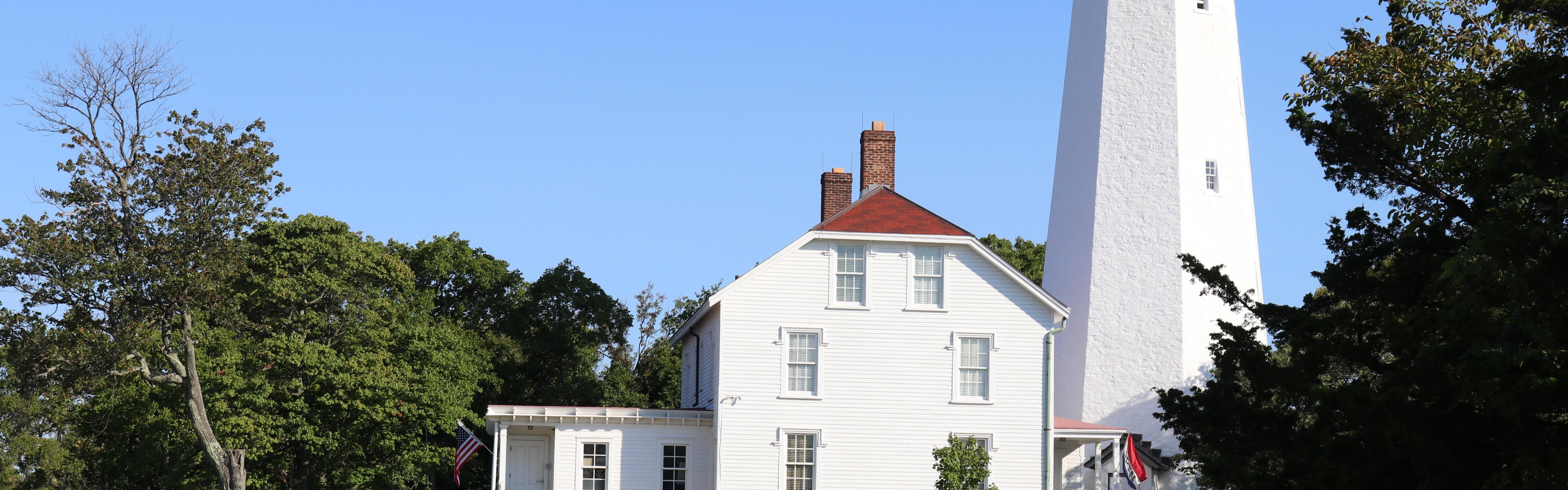 White Lighthouse and building with red roofs against blue sky