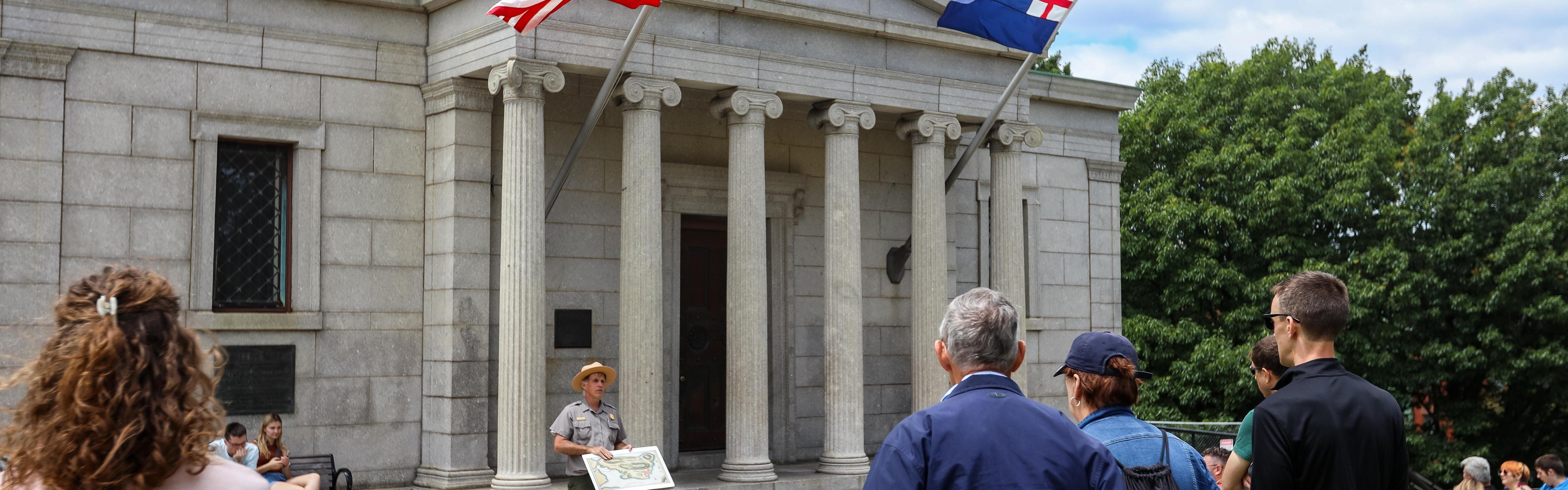A ranger stands in front of the Bunker Hill Lodge speaking to a group of people