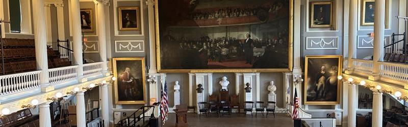 Photo of a big hall with a balcony, stairs on the floor, and artwork adorning the walls