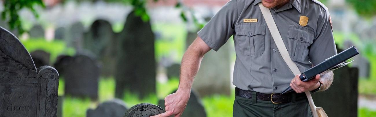 A park ranger pints out something on a historic 18th century gravestone