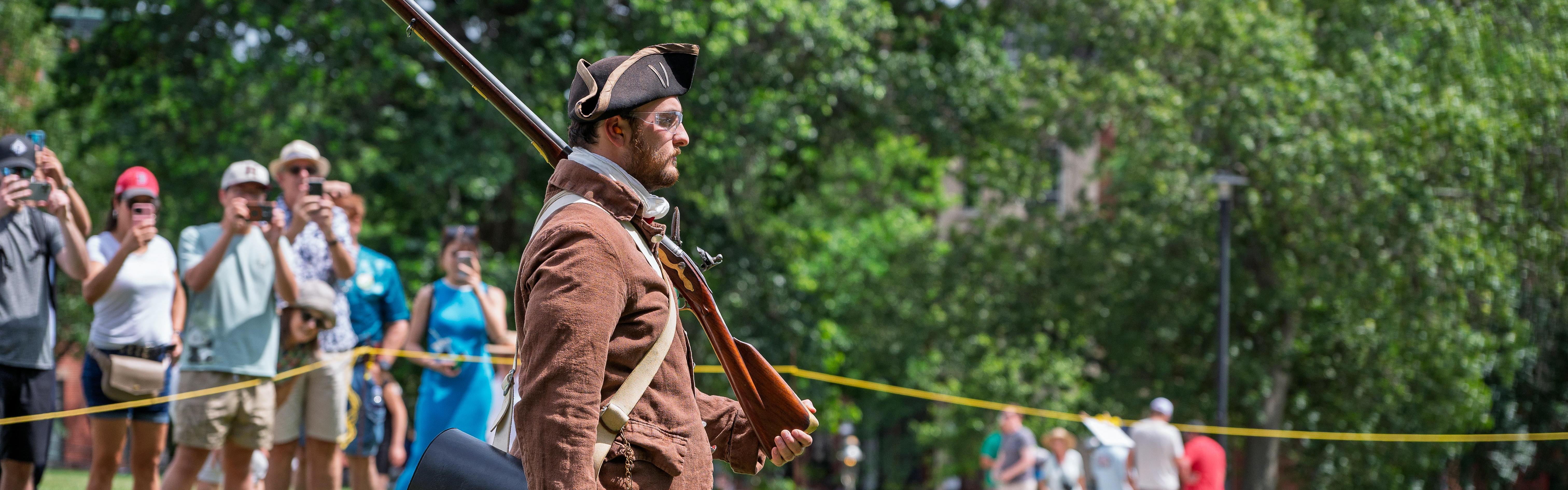 A ranger dressed in period clothing has a musket resting on his shoulder in front of an audience