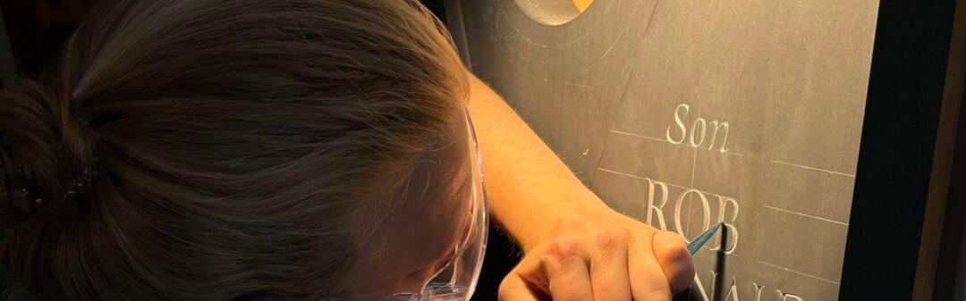 Michael Brache carving a gravestone with a chisel in dramatic low lighting