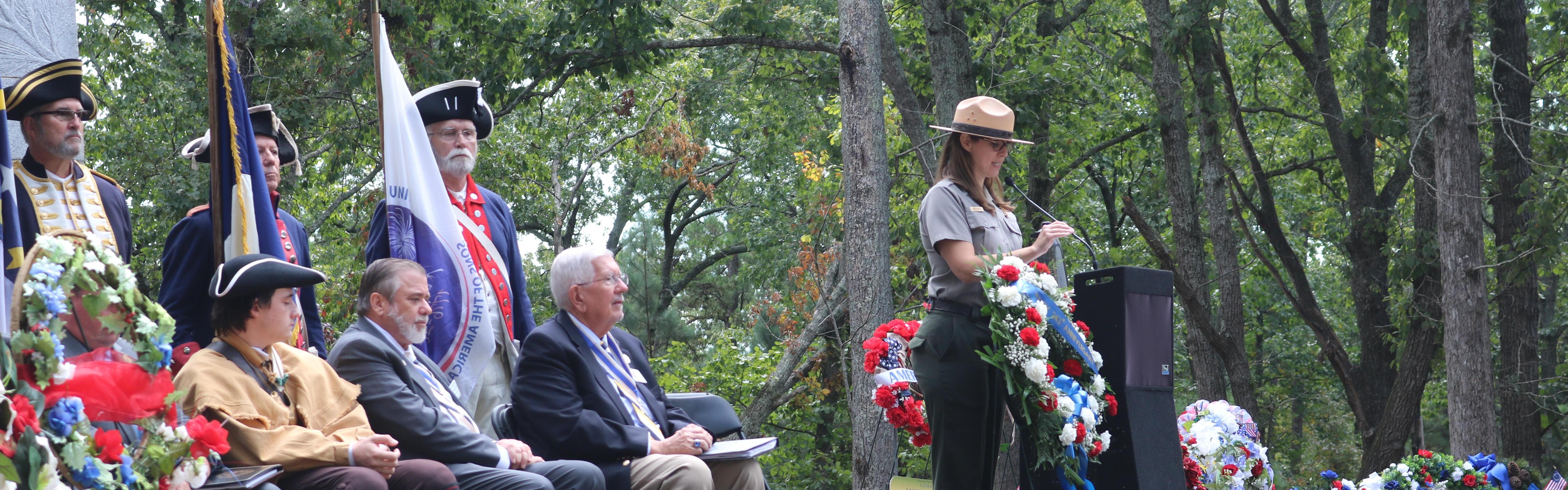 A park ranger speaks behind a podium with guests seated behind her.
