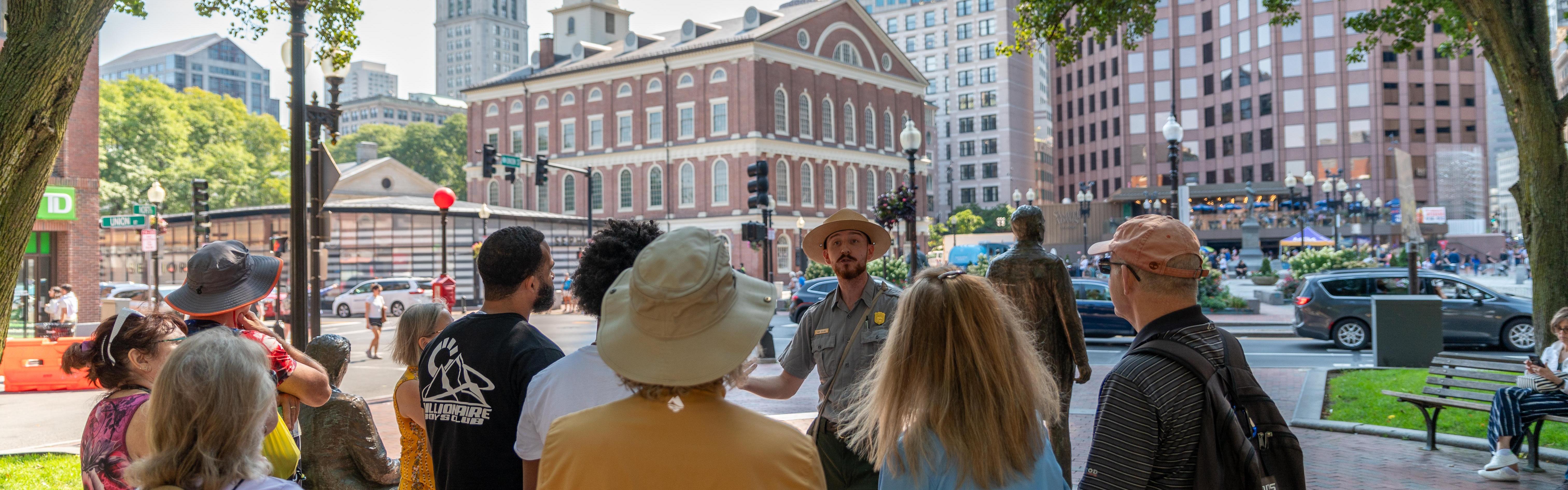 A group of people stand in front of a Ranger who is giving a tour in front of Faneuil Hall