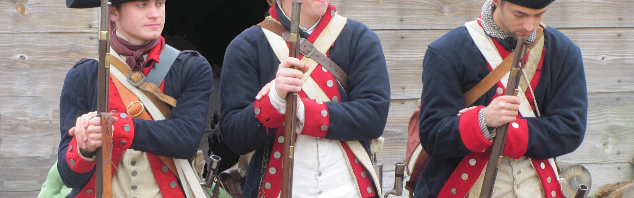 Three Continental Soldiers stand shoulder to shoulder in a relaxed stance, holding their muskets.