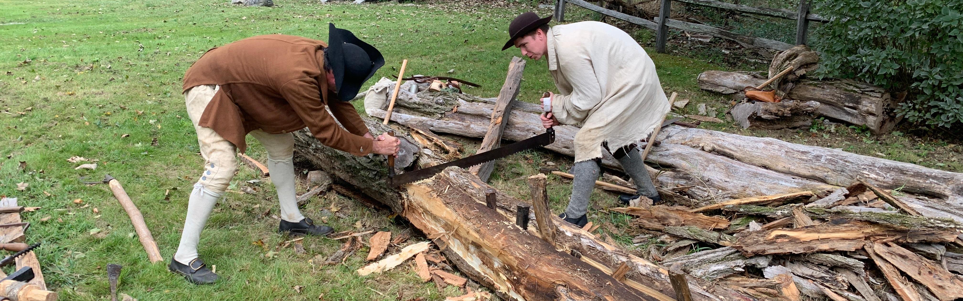 Two men dressed in historical clothing saw a large log