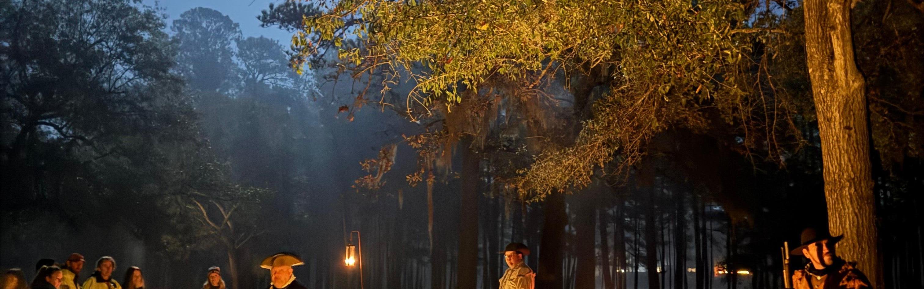 People dressed in colonial clothing outside at night with lanterns and a full moon illuminating them