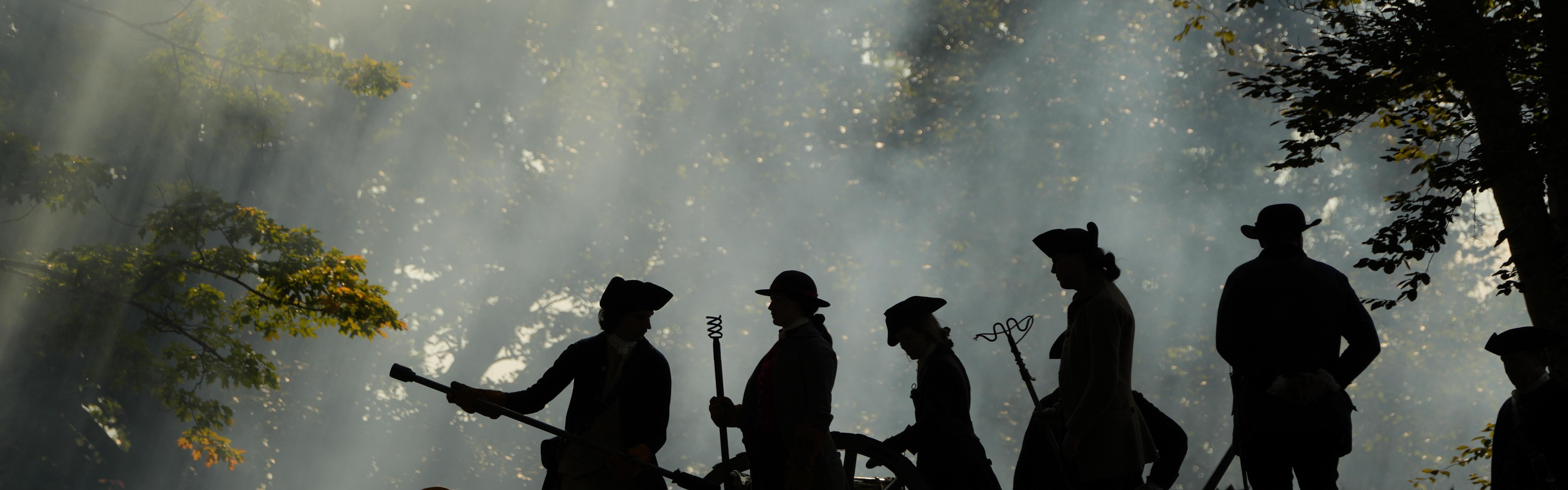 A group of people dressed as Revolutionary War artillery soldiers are working on a cannon