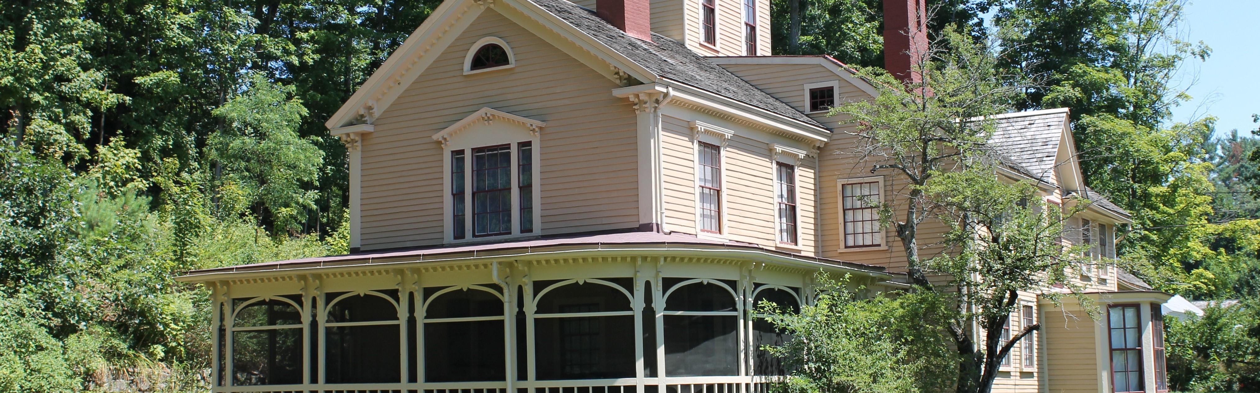 A yellow wooden house with wrap around porch and 3 story central tower