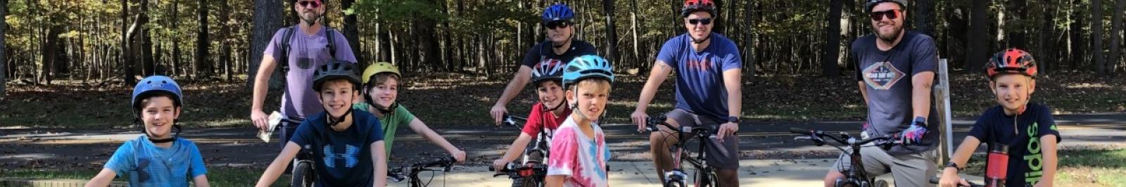Ten men and boy cyclists pose with their road bikes, wearing helmets and smiling