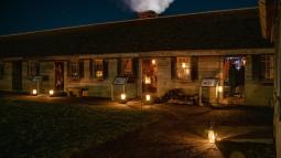 Candles in lanterns pour a golden light onto a darkened wooden building.