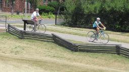 Two people cycle in a line down the park trail.