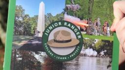 The cover of a junior ranger booklet with the wooden badge held in the lower left corner.