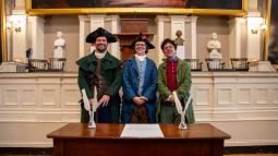 Three rangers in historic clothing stand in front of a signed resolution smiling at the camera
