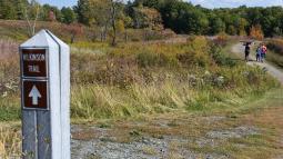Wilkinson Trail marker in foreground, trail with 3 hikers cutting through meadow
