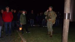 Man in WW II military uniform leading group of visitors holding lanterns