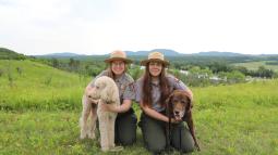 Two women in park ranger uniforms kneel next to two dogs on leash.