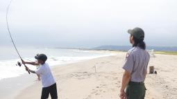 Child casting fishing rod being watched by park ranger
