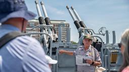 A ranger stands in front of a gun mount speaking to members of the public.