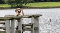 A young boy on a dock pulls a fish up with his rod.