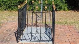 Image of an in ground tombstone with black and gold fencing surrounding