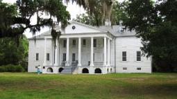 Image of the front of a large white house surrounded by trees