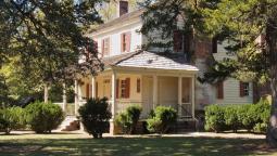 Image of a large colonial house partially hidden by pine trees