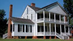 A photo of a large white colonial era three story house with columns