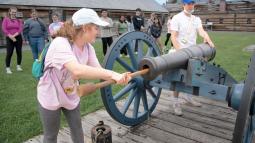 Two young people swab a cannon while standing in formation.