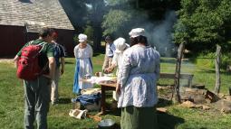 Women in colonial clothing giving a demonstration to tourists.