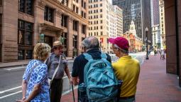 A ranger stands in front of the old state house with a crowd of visitors around him