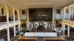 Photo of a big hall with a balcony, stairs on the floor, and artwork adorning the walls