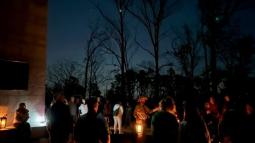 A park ranger in a flat hat speaks to a group of people at night with stars and trees behind.