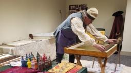 a man in colonial dress hand-coloring paper