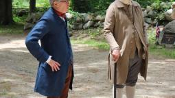 Two men in colonial clothing stand along a dirt road.