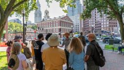 Visitors stand in front of a Ranger leading a tour, Faneuil Hall is in the background