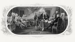 Men gathered in a large room several gathered around a small desk covered in papers.