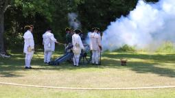 Group of living historians in white hunting frocks fire a cannon