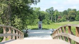 Standing in the middle of a wooden bridge with railings on either side, looking toward a statue.