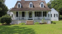 White 1-1/2 story wood house with porch extending across main house with brick stairs in the center