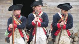 Three Continental Soldiers stand shoulder to shoulder in a relaxed stance, holding their muskets.