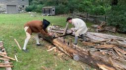 Two men dressed in historical clothing saw a large log