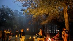 People dressed in colonial clothing outside at night with lanterns and a full moon illuminating them
