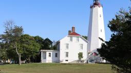 White Lighthouse with red top beside white building with red roof.