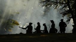A group of people dressed as Revolutionary War artillery soldiers are working on a cannon