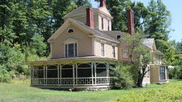 A yellow wooden house with wrap around porch and 3 story central tower